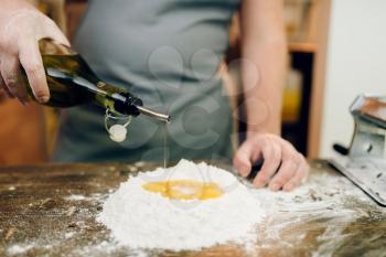 Homemade pasta cooking, man adds oil to the flour on wooden kitchen table. Traditional italian cuisine