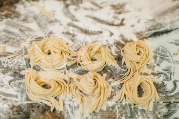 Uncooked homemade fettuccine on wooden kitchen table sprinkled with flour closeup, nobody. Fresh pasta preparation