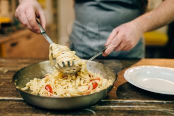 Male chef cooking pasta, pan on wooden kitchen table. Homemade fettuccine preparation process. Traditional italian cuisine