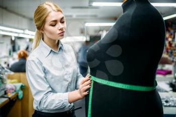 Clothes designer measures a dress on mannequin, manufacture on sewing factory. Garment measuring, seamstress, dressmaking or tailoring