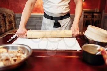 Male chef roll out the dough with a rolling pin on wooden table. Homemade strudel cooking