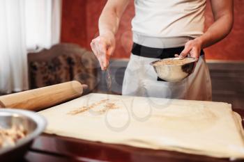 Male chef cooking apple strudel on the kitchen, ingredients on background. Homemade sweet dessert, preparation process