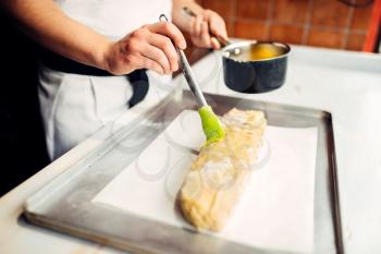 Male chef hand lubricates apple strudel with egg and butter. Homemade sweet dessert cooking, preparation process
