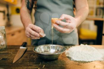 Pasta cooking process, male chef hands with egg, a bunch of flour on wooden table