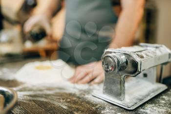 Pasta machine, male chef preparing dough on wooden kitchen table. Homemade spaghetti cooking