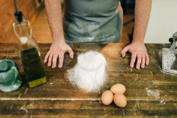 Male chef in apron, flour and eggs on wooden table. Homemade pasta cooking