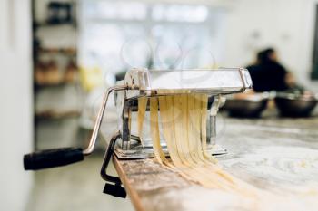 Pasta machine with dough on wooden kitchen table sprinkled with flour closeup, nobody. Traditional italian cuisine