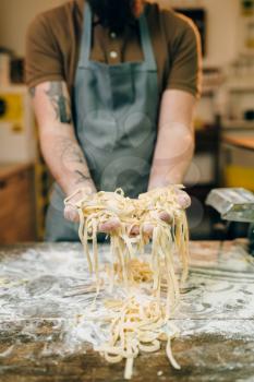 Male chef hands with uncooked homemade pasta, wooden kitchen table sprinkled with flour. Fettuccine preparation process