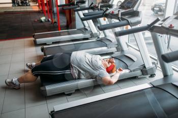 Overweight tired woman lies on a treadmill after running in gym. Calories burning, obese female person in sport club
