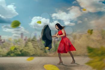 Young woman in red dress with black umbrella in hurricane. Female person with parasol in bad weather