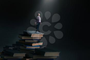 Little young woman standing on mountain of large books and textbooks, scale effect. Knowledge and education, reaiding concept
