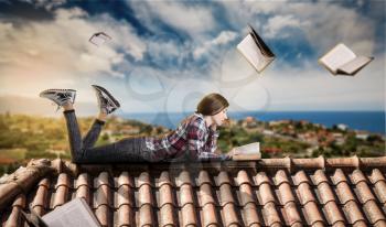 Young woman reads while lying on the top of the roof, books fly around. Gaining knowledge and education concept. Student reading
