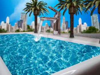 Tap water flows into the outdoor pool from faucet at sunny summer day, blue sky and modern cityscape on background