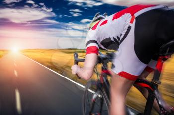 Cyclist in helmet and sportswear rides on bicycle, speed effect, back view. Workout on bike path, cycling