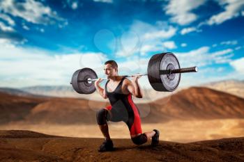 Muscular weightlifter doing squats with a barbell, deadlift, sandy desert valley on background. Weightlifting workout outdoor, bodybuilding training