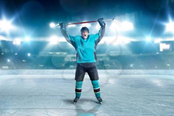 Hockey player raised his hands up, winner threw the puck into the goal, spotlights on background. Male person in helmet, gloves and uniform in ice arena