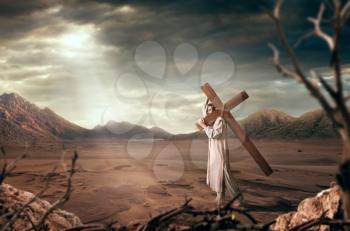 The great martyr with cross in desert, cloudy sky with sun rays. Crucifixion of Jesus Christ, symbol of christian religion