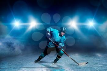 A hockey player on ice, spotlights on background. Male person in helmet, gloves and uniform holds stick in hands