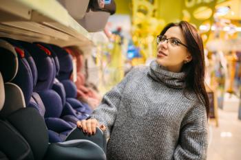 Pregnant woman choosing child car seat in store. Goods for safe children transportation