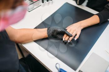 Beautician in gloves holds polishing machine and cleans old varnish from nails of female client, top view, manicure in beauty salon. Manicurist doing hands care cosmetic procedure