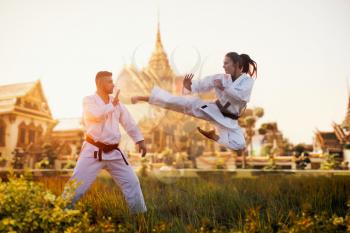 Female karate fighter trains kick in flight with master, training against ancient temple. Martial art fighters on workout outdoor, technique practice. Photo manipulation with background