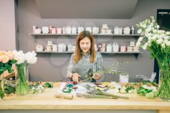 Female florist prepares flower composition, garden equipment on workplace. Flower shop, floral business