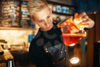 Young male barista in apron checks the sediment in the coffee pot. Barman works in cafeteria, bartender prepares espresso