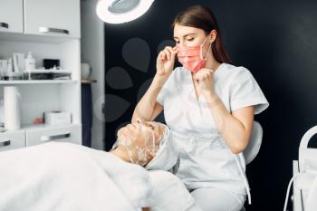 Beautician watches on patient face in mask, getting rid of wrinkles, cosmetology clinic. Facial skincare, rejuvenation procedure in spa salon, health care