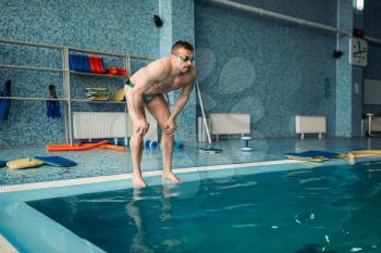 Male swimmer in goggles prepares to jump into the water, workout in swimming pool