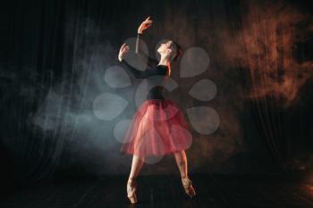 Ballet dancer in red dress dancing on the stage in theatre. Graceful ballerina training in class