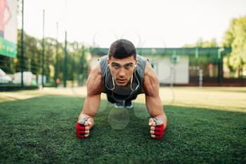 Athletic man doing push-up exercise on a grass, outdoor fitness workout. Muscular sportsman on sport training in summer park