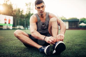 Man prepares for outdoor fitness workout. Sportsman sitting on the grass and tying shoelaces on sneakers