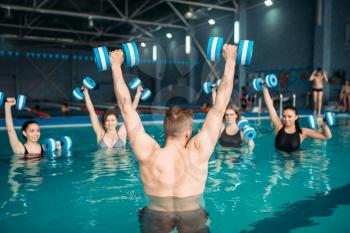 Female class with trainer on workout with aqua dumbbells in swimming pool. Women in swimwear on training, water sport