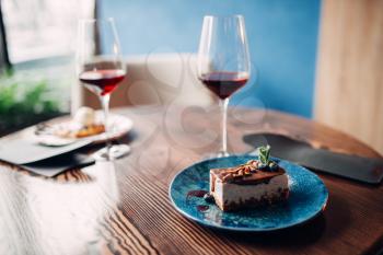 Dessert on a plate and red wine in glass on wooden table, nobody. Chocolate cake and alcohol, arrangement of romantic dinner in cafe