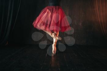 Female ballet dancer legs in pointes. Ballerina in red dress and black practice dancing on the stage in theatre