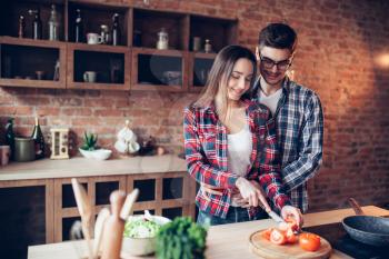Husband hugs wife while she cooking fresh vegetable salad in bowl on the kitchen. Diet food preparation. Couple prepares romantic dinner, healthy lifestyle