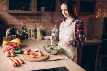 Female cook holds wooden spoon, vegetable salad cooking on the kitchen. Fresh diet food preparation. Wife prepares romantic dinner for her husband