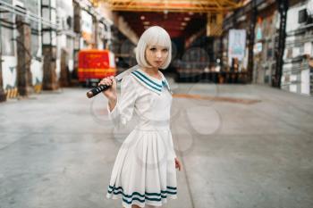 Pretty anime style blonde girl with sword poses on abandoned factory. Cosplay fashion, asian culture, doll with blade, cute woman with makeup