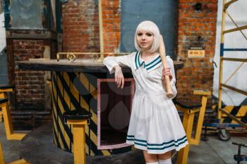 Cute anime style blonde lady with baseball bat. Cosplay fashion, asian culture, doll in dress, sexy woman with makeup in the factory shop