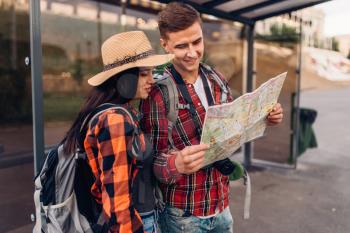 Couple at bus stop study the map of city attractions, excursion in tourist town. Summer hiking. Hike adventure of young man and woman