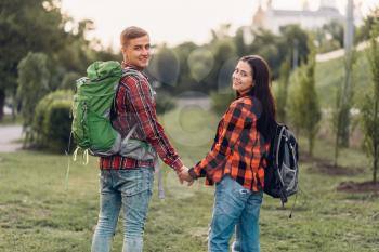 Love couple of tourists with backpacks holding hands, happy vacation. Summer adventure of young man and woman, walking in city park