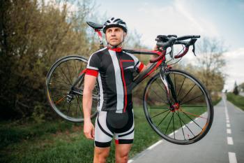 Bycyclist in helmet and sportswear keeps the bike on shoulder after biking on asphalt road. Male sportsman rides on bicycle. Workout on bike path