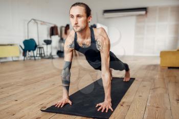 Male yoga with tattoo on hand doing push up exercise in gym with grunge interior. Fitness workout indoors