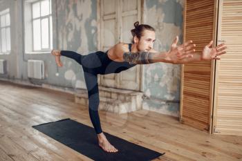 Male yoga with tattoo on hand doing stretching exercise on mat in gym with grunge interior. Fit workout indoors