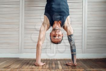 Yoga standing on hands, upside down exercise. Male athlete on fitness workout indoors