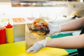 Chef puts burger in to the cardboard package, fast food cooking. Hamburger preparation process, fastfood