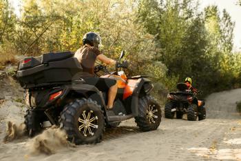 Two quad bike riders in helmets travels in forest, front view. Riding on atv, extreme sport and travelling, quadbike adventure