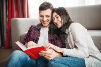 Happy love couple sitting on the floor and looks at the book together. Modern apartment interior of living room on background
