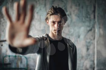 Young man with a cigarette in his mouth reaching his hand forward, grunge background. No smoking concept, drug addict