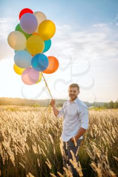 Happy man with bunch of balloons walks in wheat field